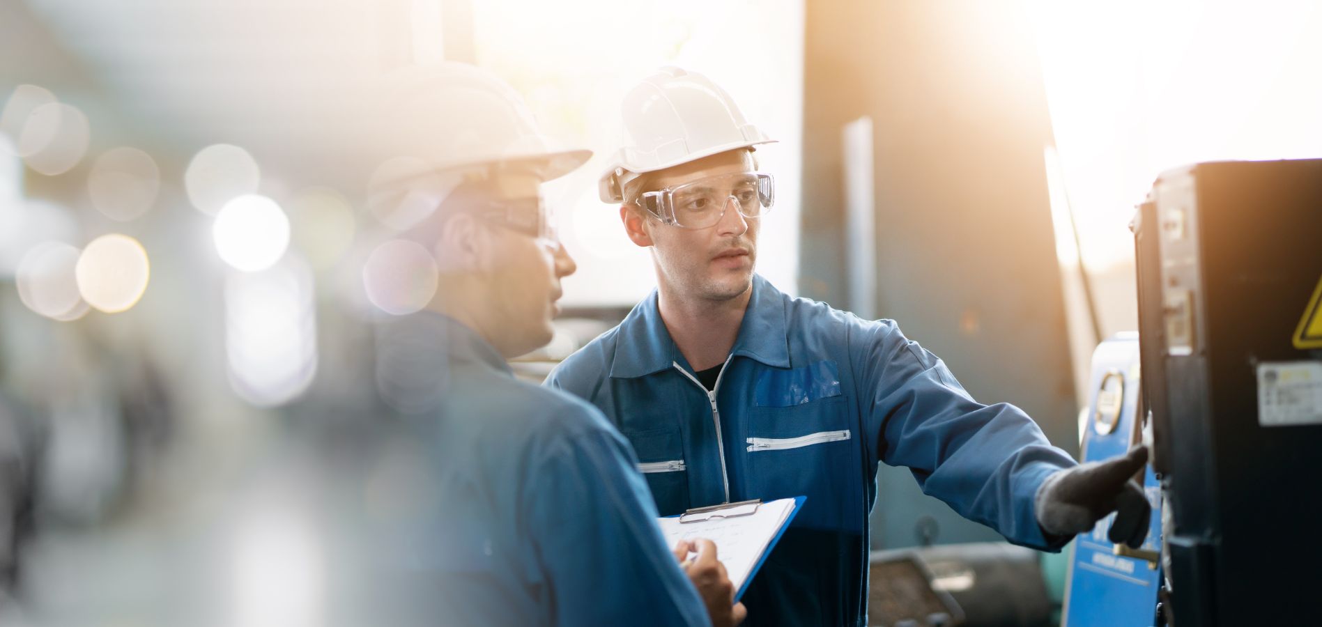 Monteur met helm bedient machine terwijl collega meekijkt met klembord