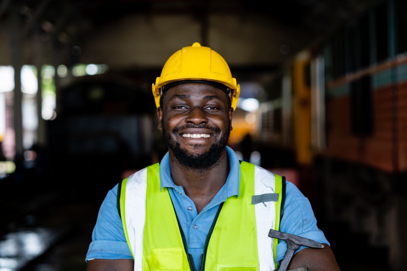 Lachende man met gele helm en hamer bij trein