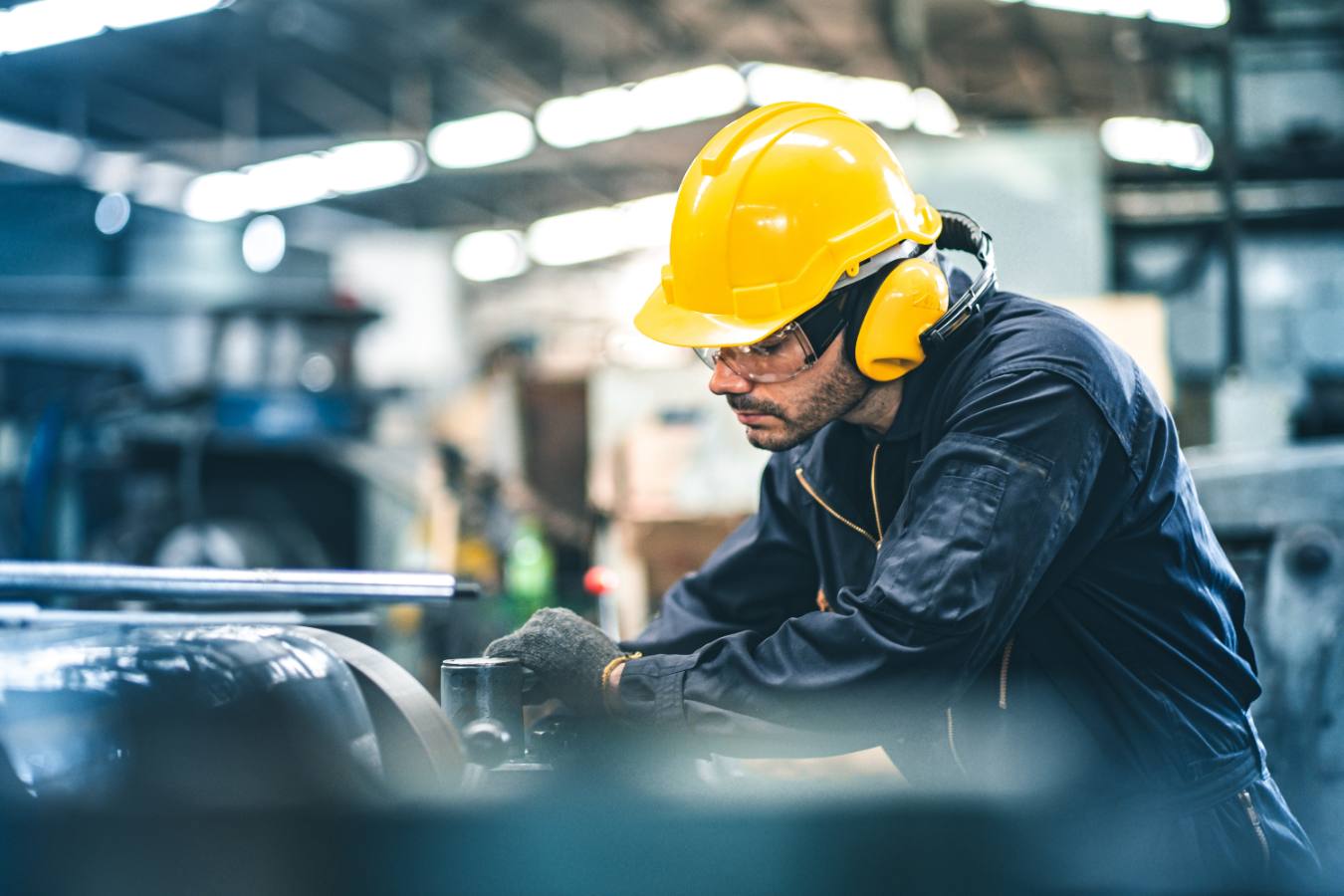 Monteur met gele helm en gehoorbescherming werkt aan machine