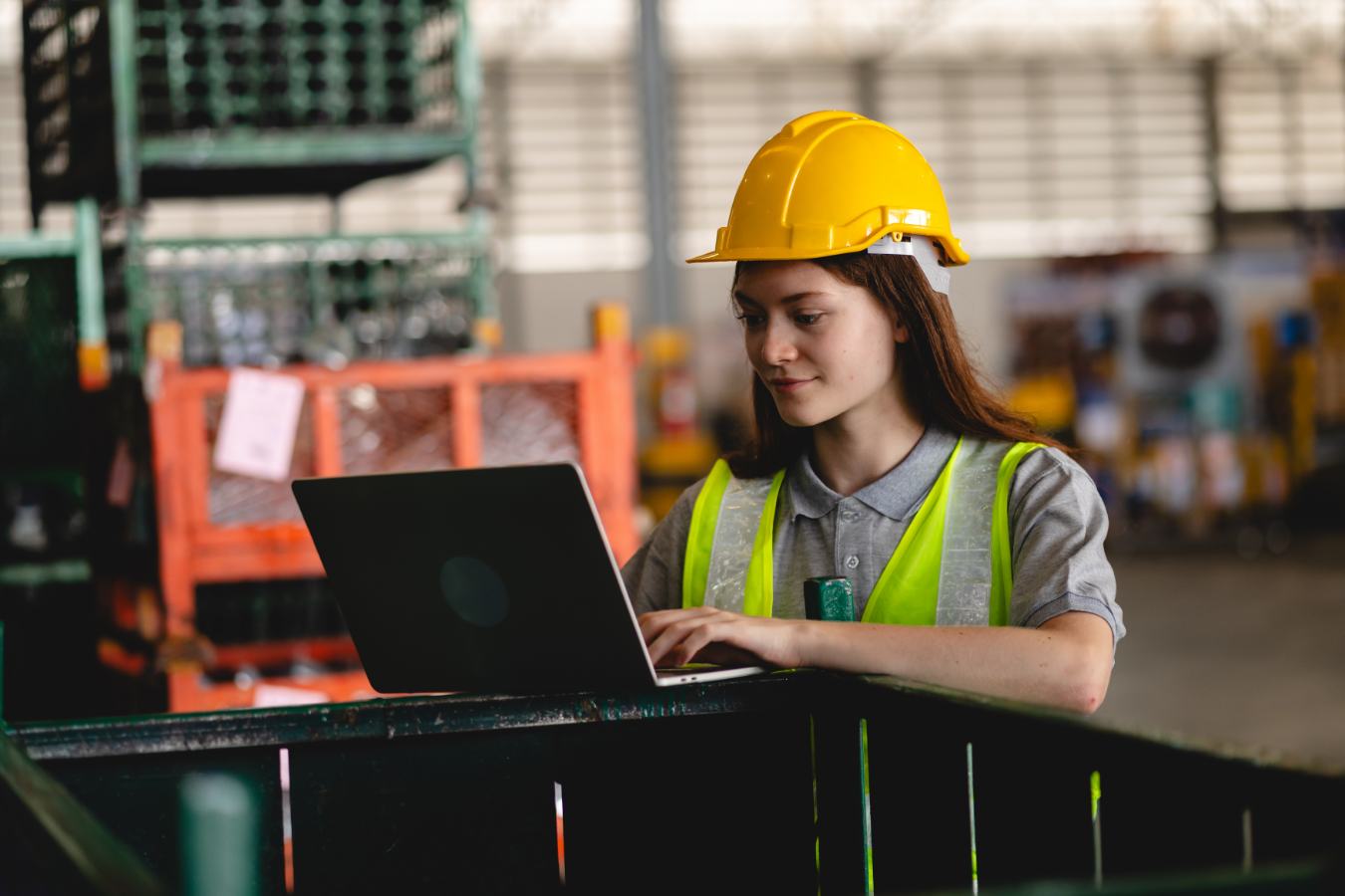 Vrouw met gele helm werkt aan laptop in magazijn