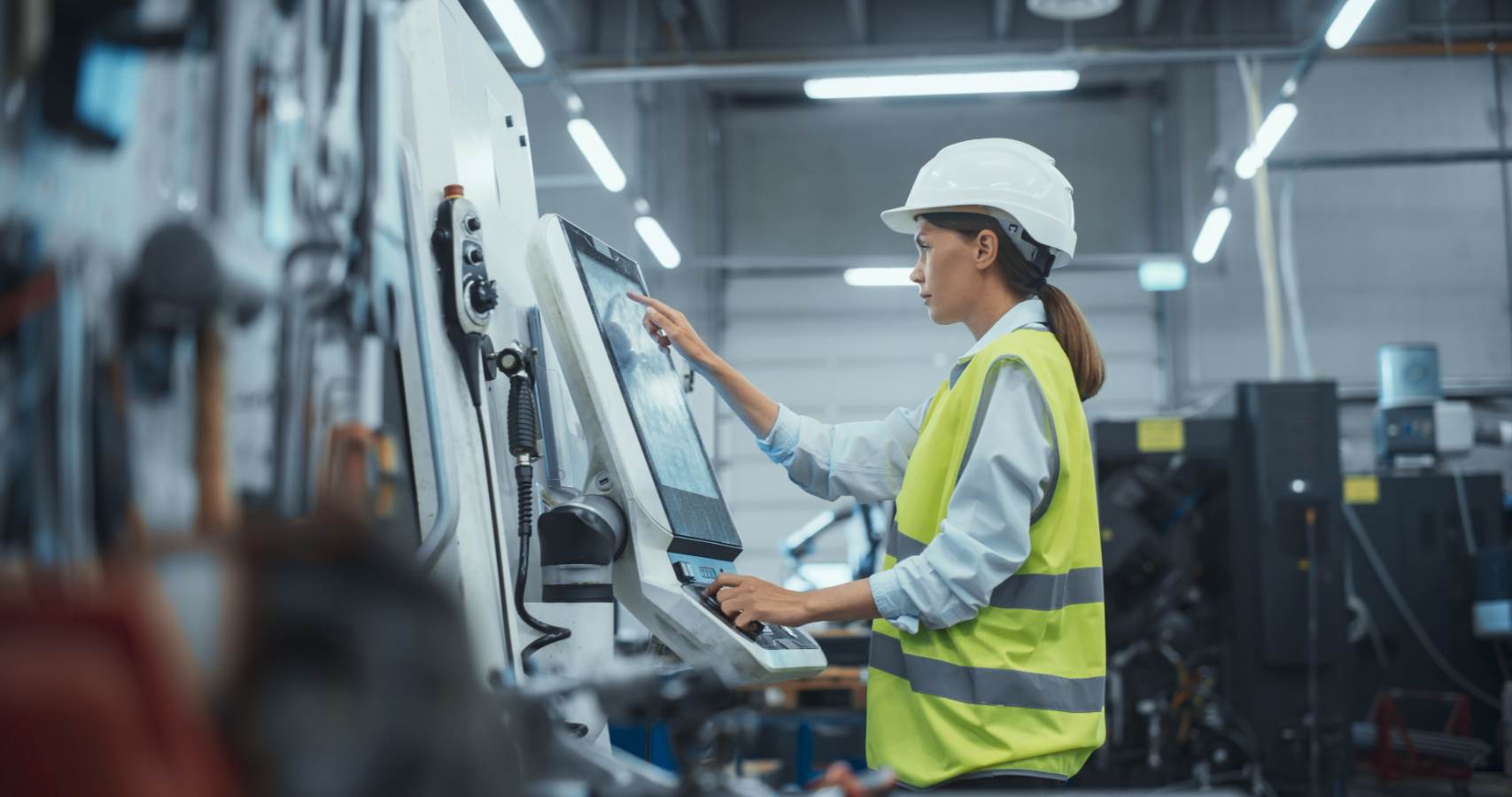 Vrouw met helm bedient touchscreen van machine in werkplaats