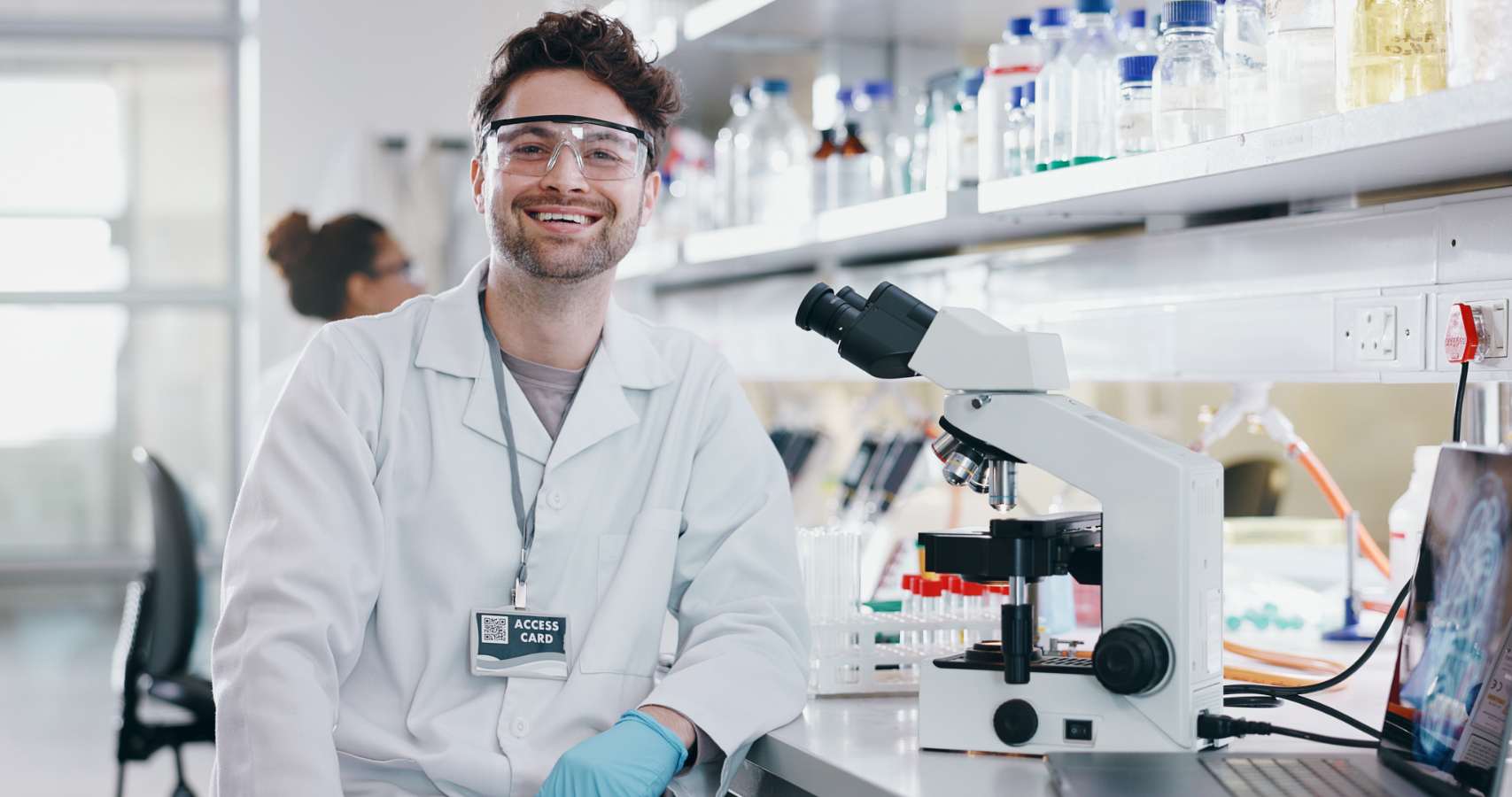 Lachende labmedewerker met veiligheidsbril naast microscoop