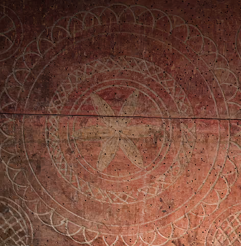 Close-up of reddish-brown surface with a circular, floral-like pattern featuring a central five-petal flower and concentric rings decorated with geometric designs.