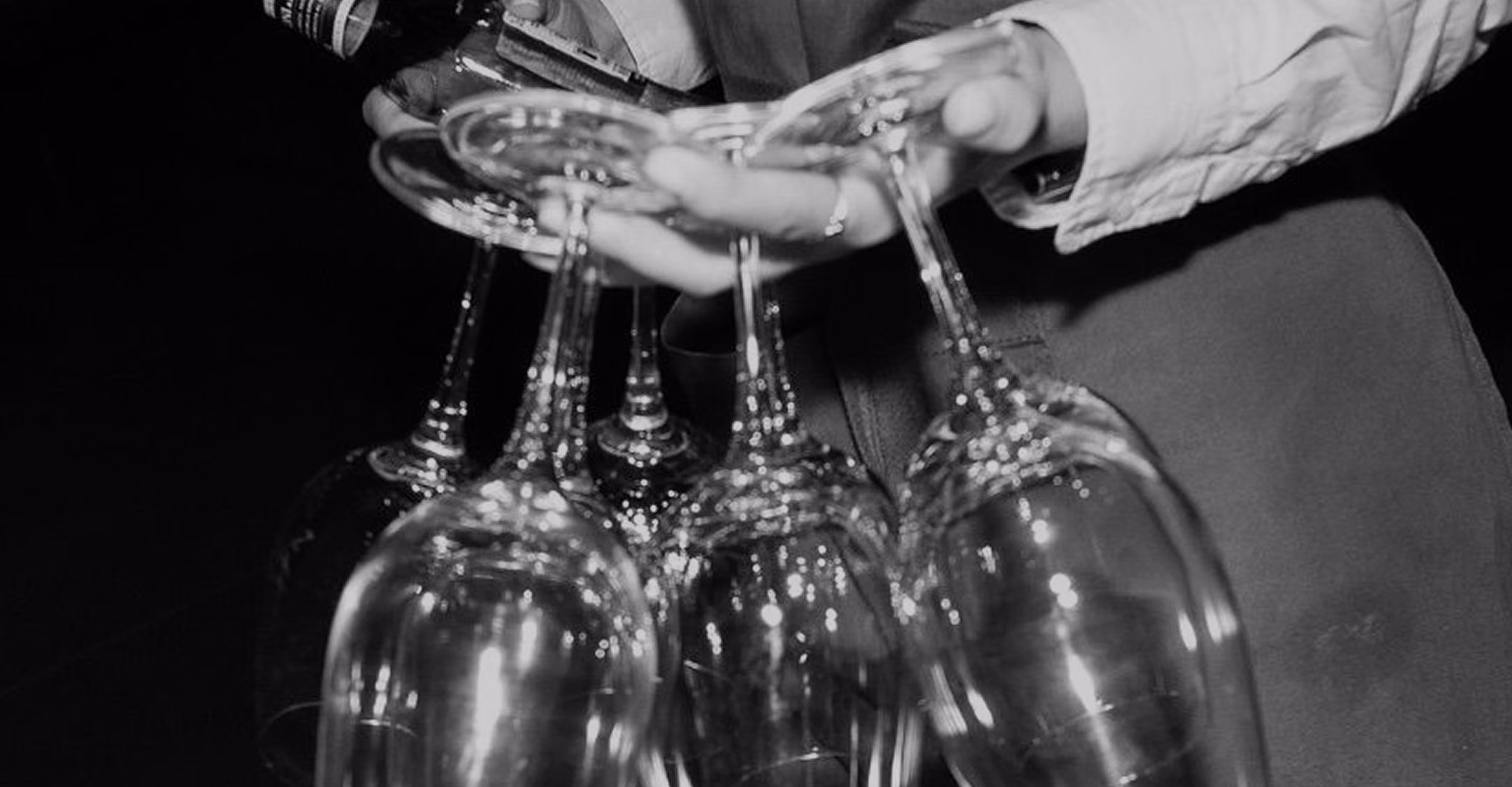 Person holding multiple empty wine glasses by their stems in one hand.