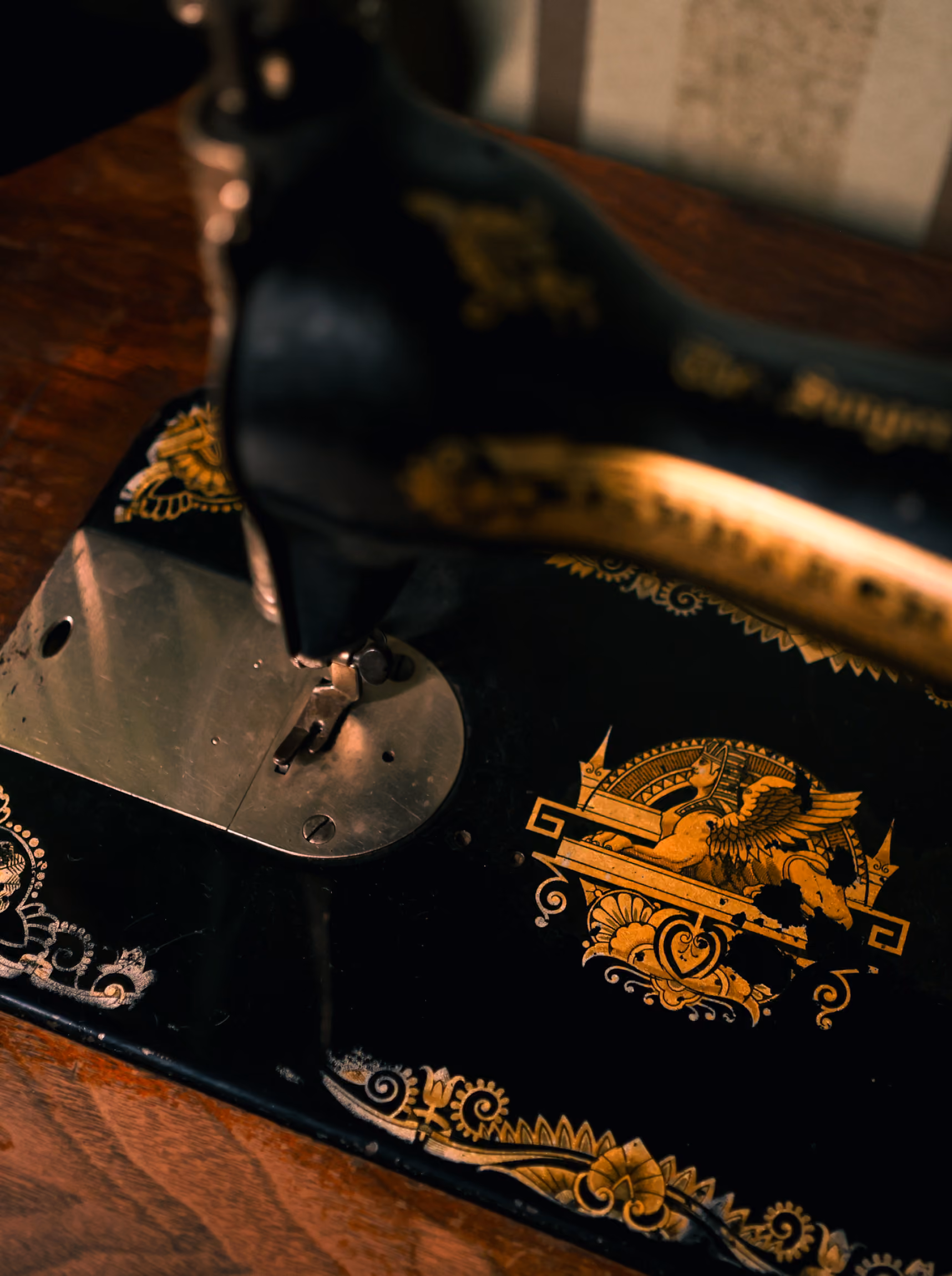 Close-up of a vintage black sewing machine with ornate gold decorative designs, including a winged lion emblem, on a wooden surface.