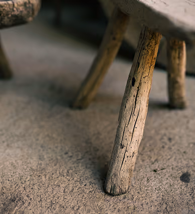 Close-up of rustic wooden chair legs resting on a textured concrete floor, showing natural cracks and wood grain.