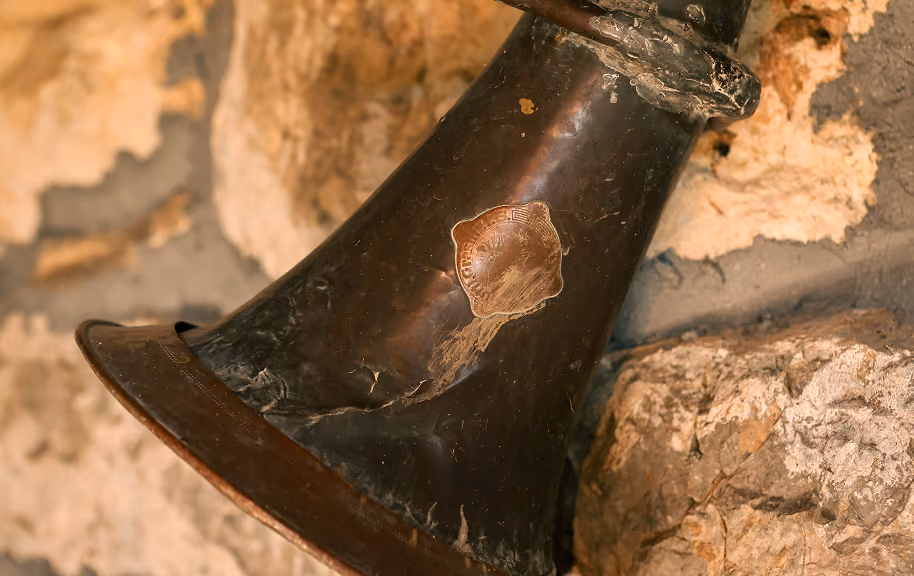 Close-up of an old, worn-out black horn with visible scratches and a faded circular emblem, resting against a rough stone wall.