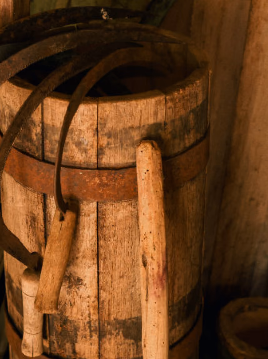 Close-up of an old wooden barrel with rusty metal bands, holding a couple of curved hand tools with wooden handles.