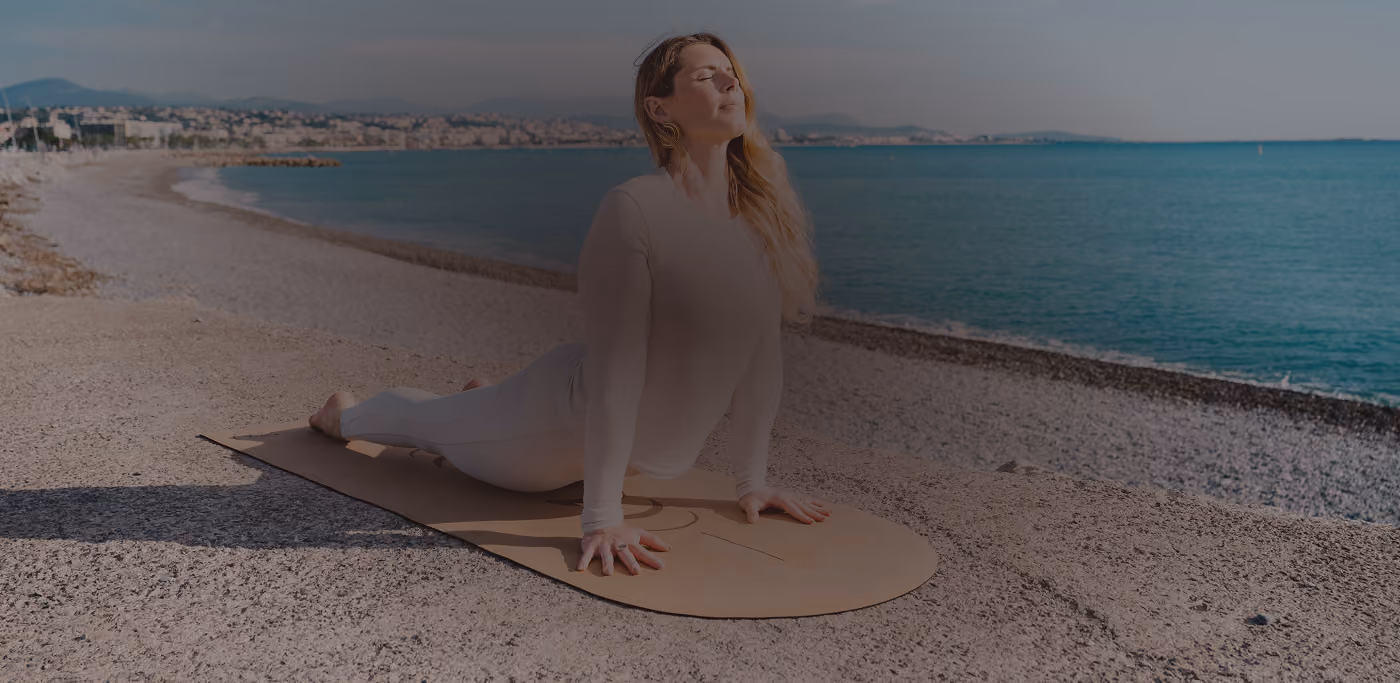 Femme en tenue blanche en posture de yoga sur un tapis, au bord de la mer