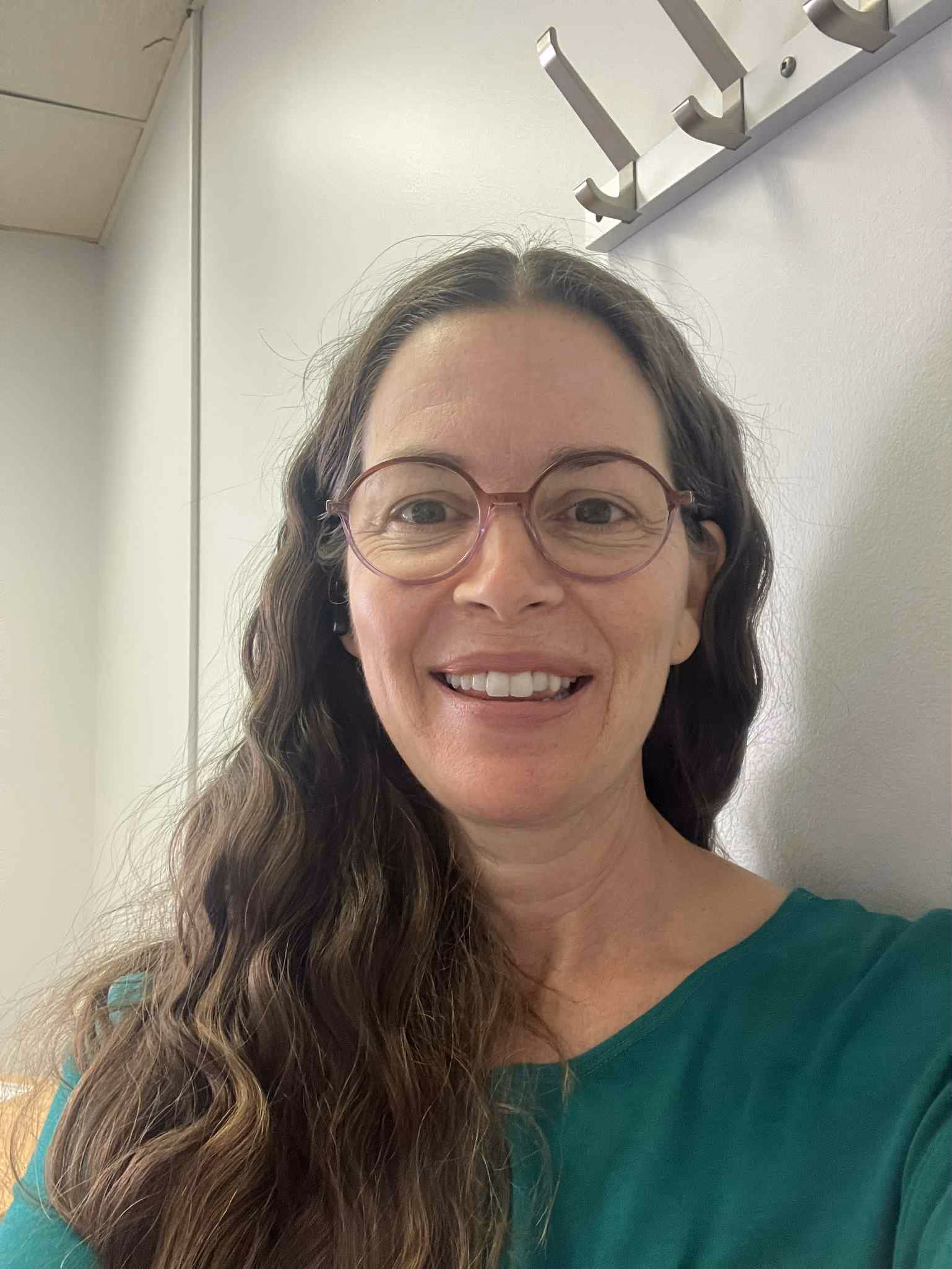 Femme souriante aux cheveux longs ondulés et lunettes, en haut vert