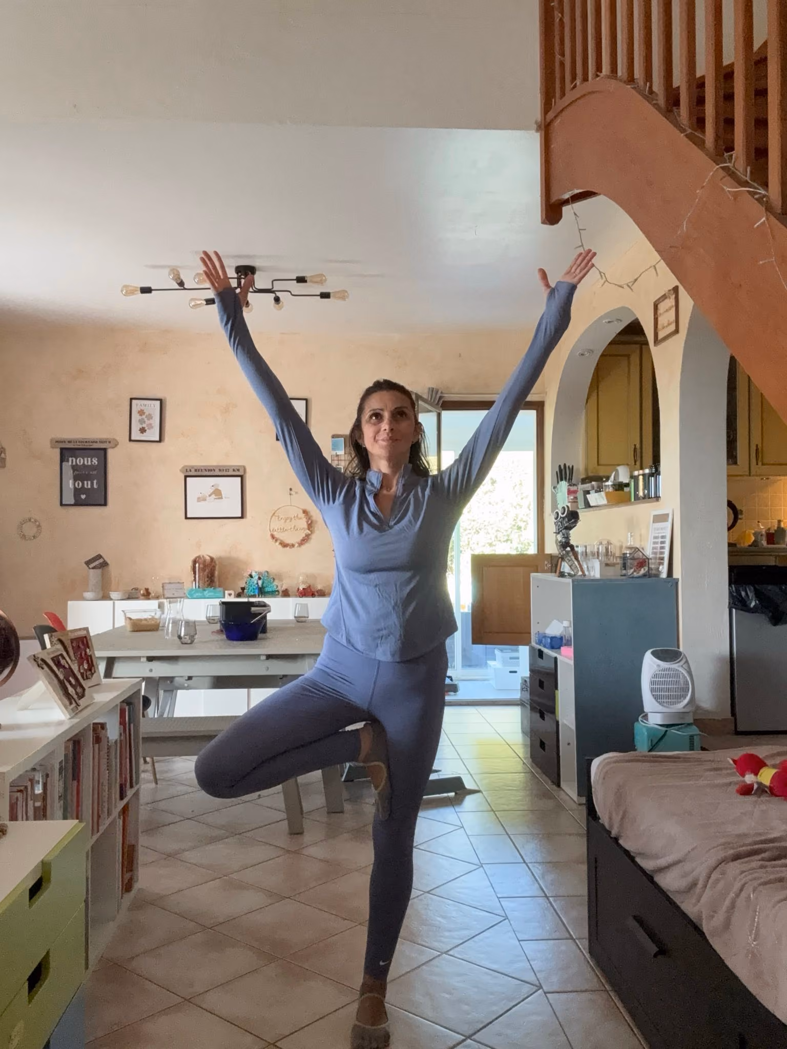 Femme en tenue de sport bleue en posture de l'arbre, bras levés
