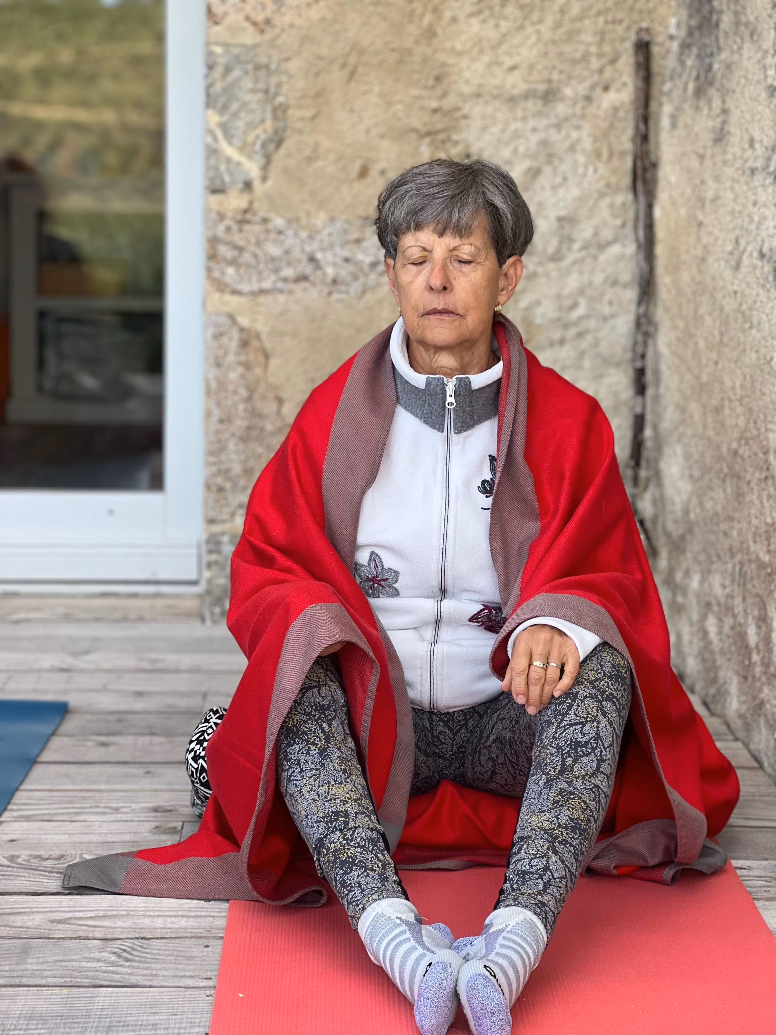 Femme assise en méditation sur un tapis de yoga, enveloppée dans un plaid rouge