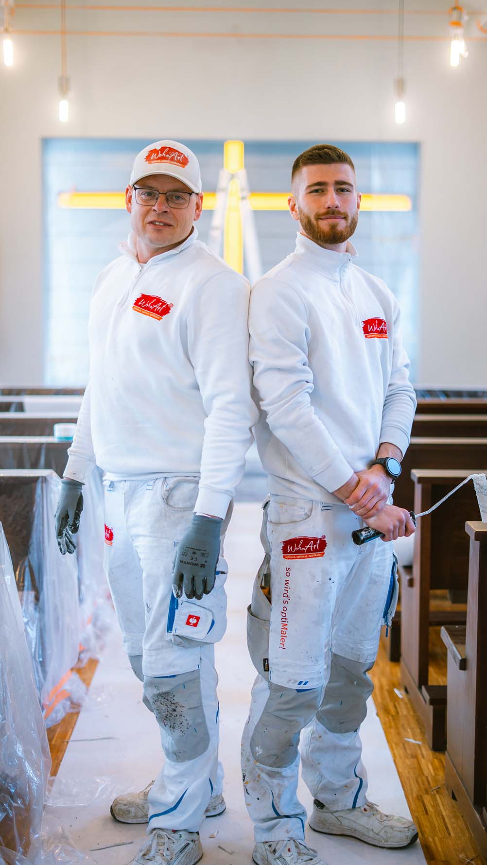 Zwei WohnArt-Maler in weißer Arbeitskleidung bei Malerarbeiten in einem Kirchenraum