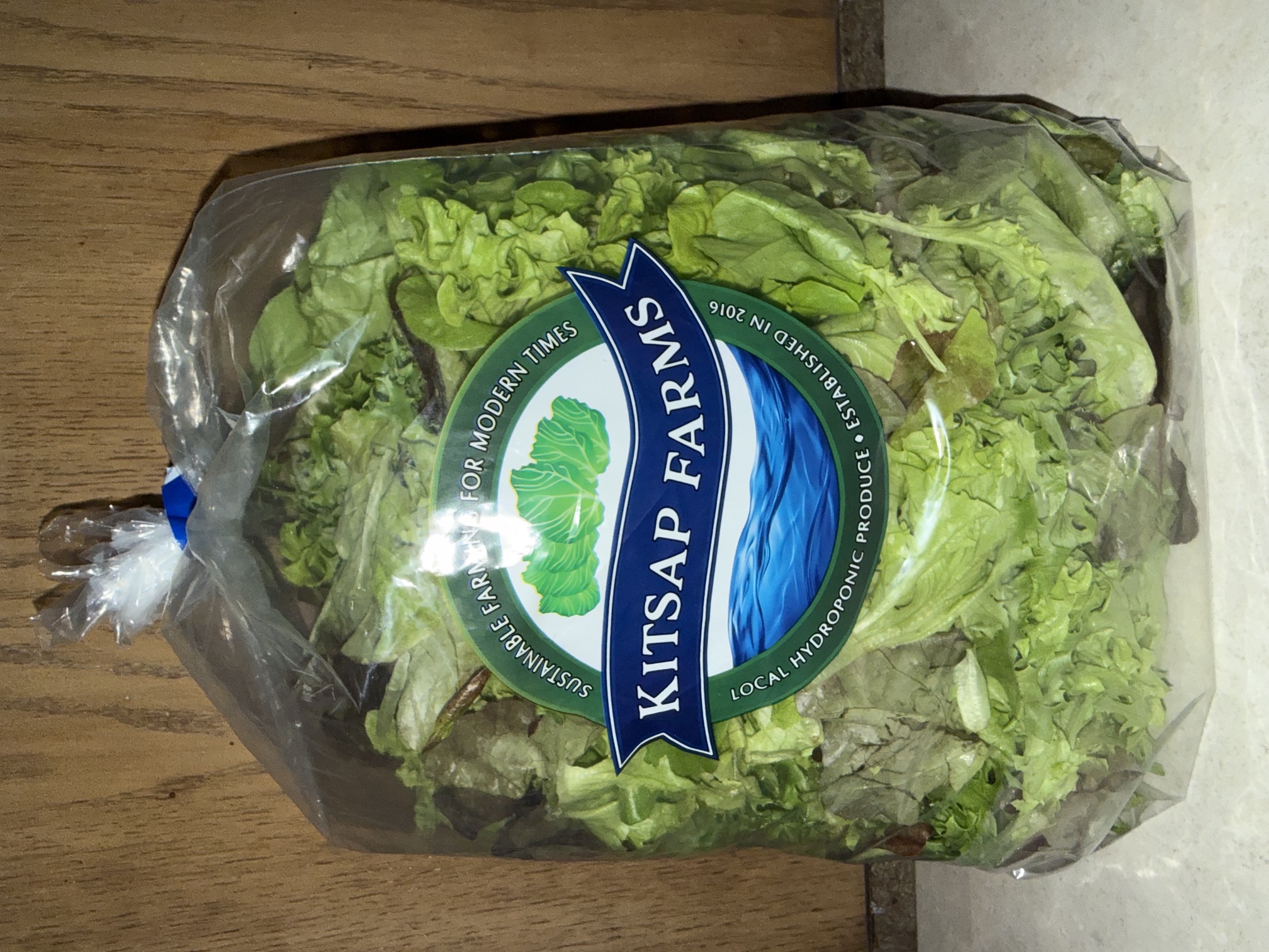 Bag of Kitsap Farms Oakleaf Mix salad greens with the farm's logo label in a store cooler