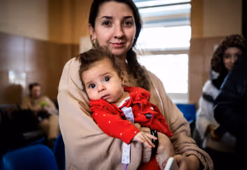 Woman holding a baby in a red outfit in a clinic waiting room