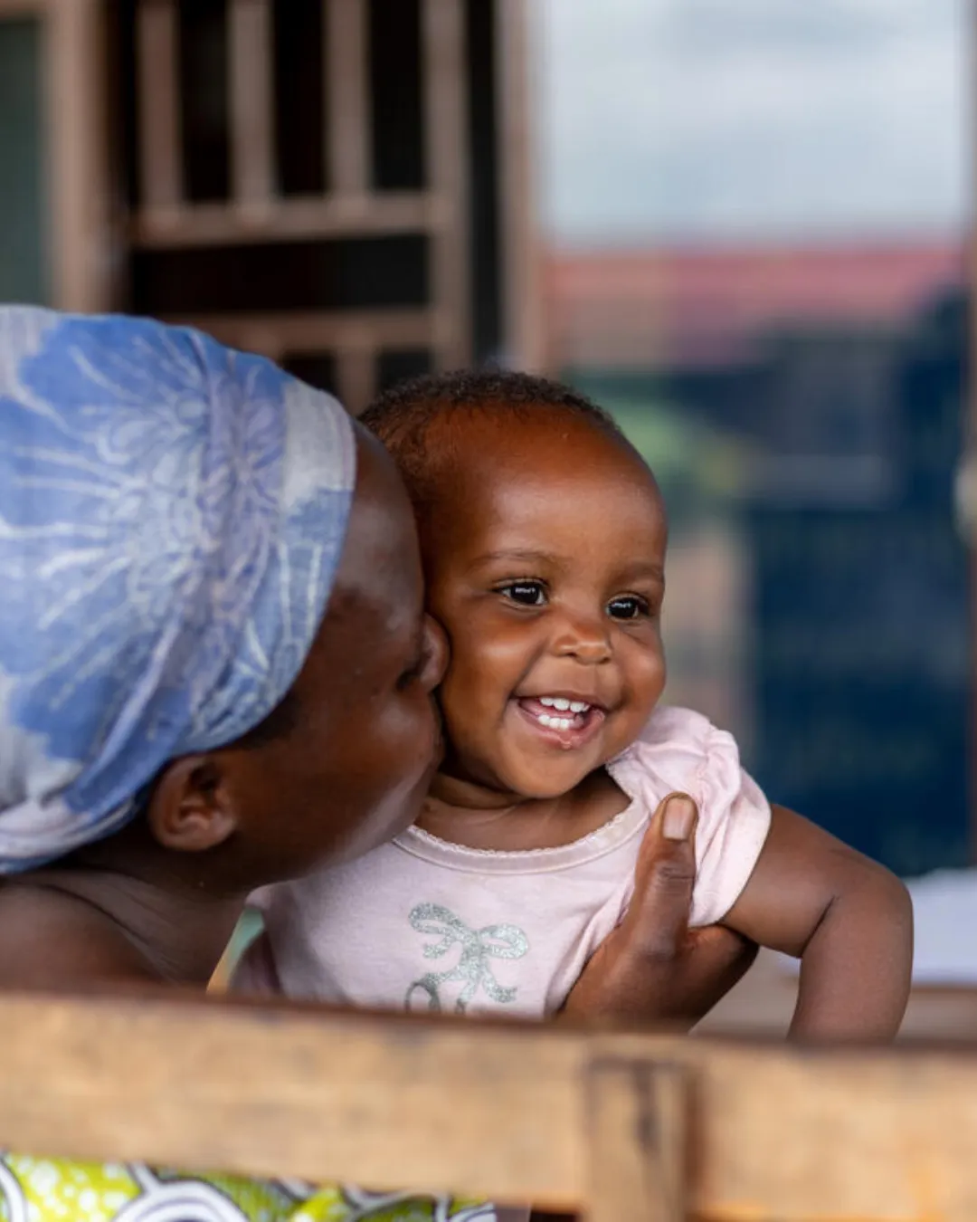 Woman in a blue headscarf kissing the cheek of a smiling baby