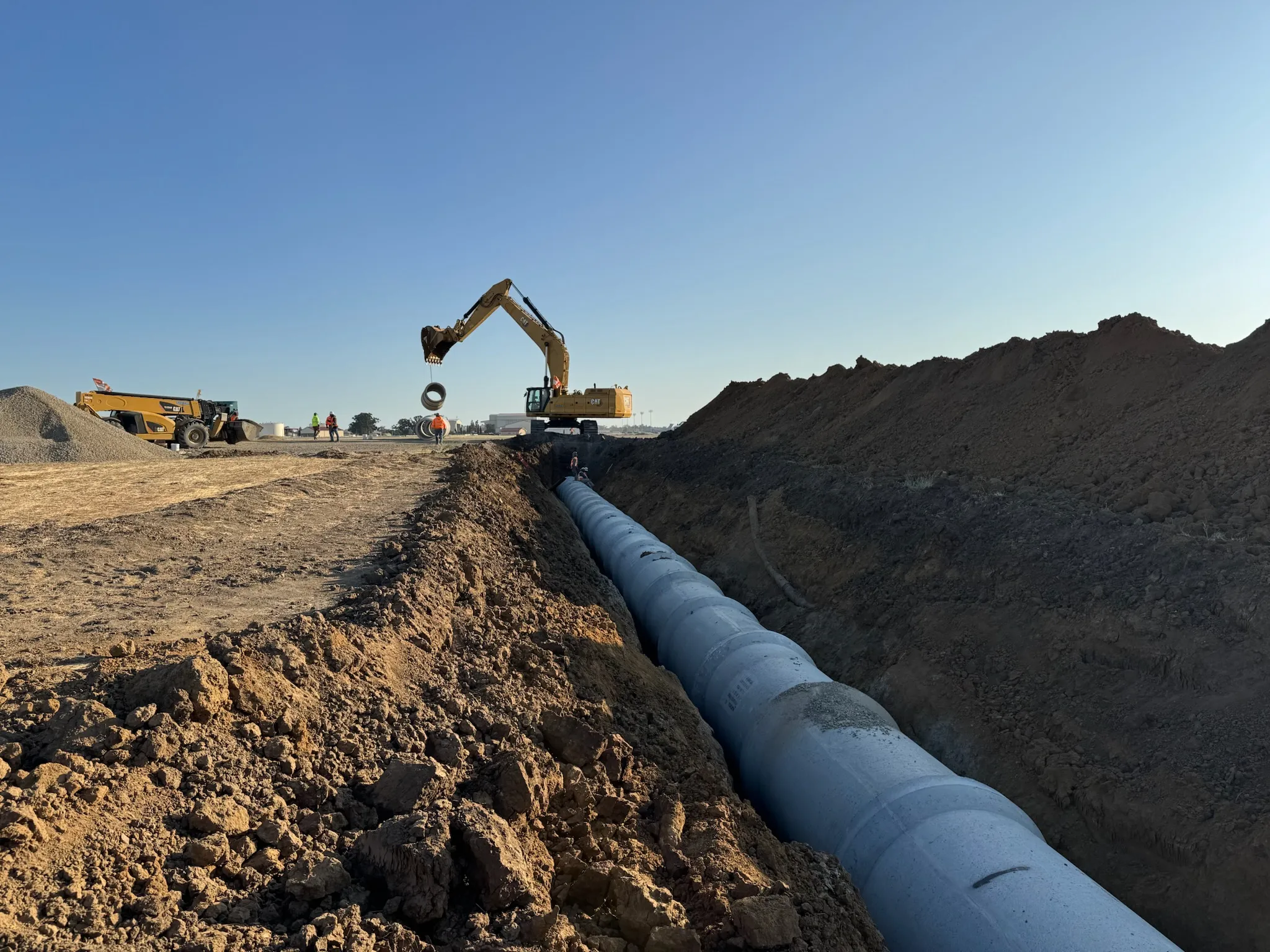Large diameter pipe laid in an open trench with an excavator working nearby