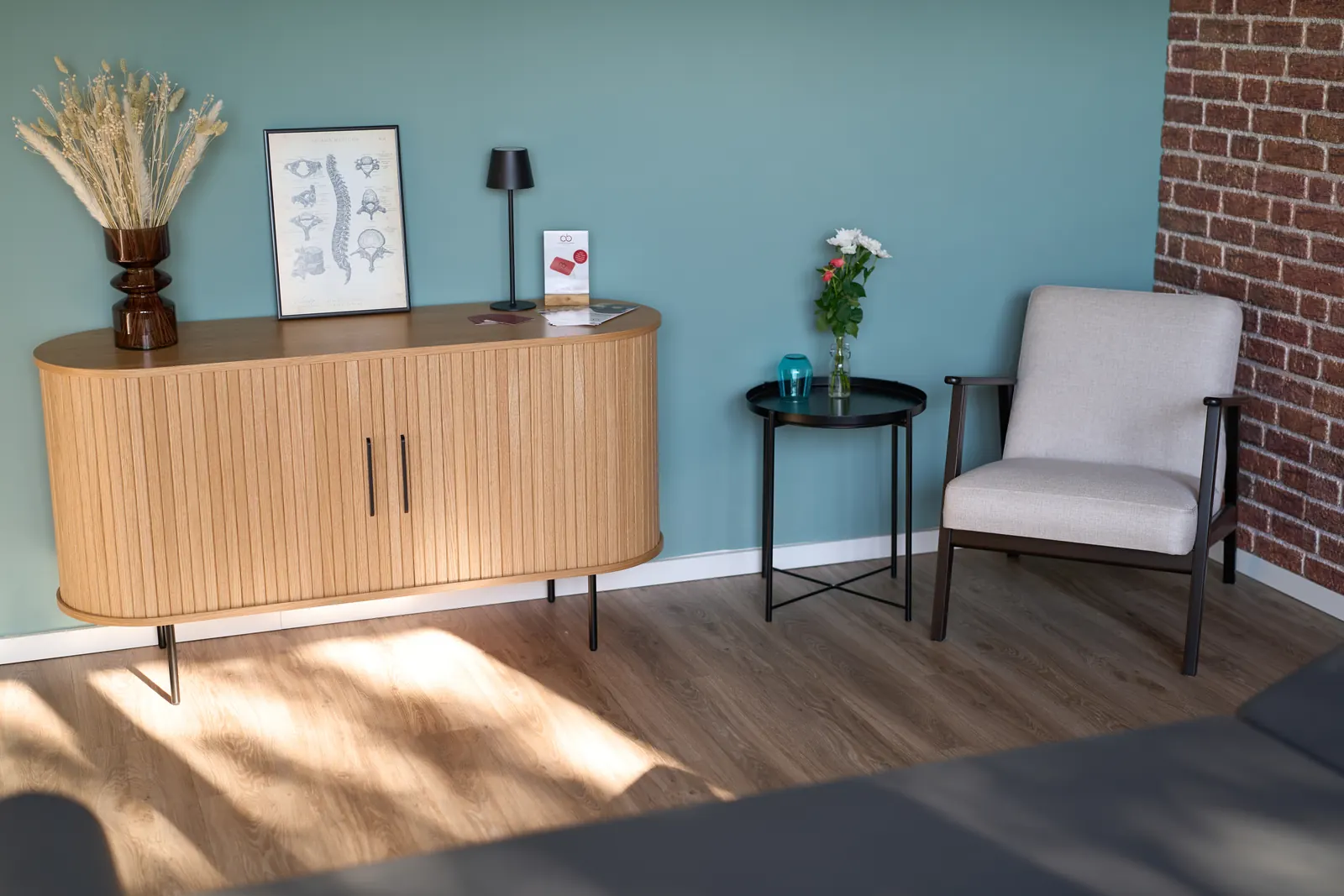 Wartebereich mit Holz-Sideboard, Beistelltisch und Sessel vor blauer Wand