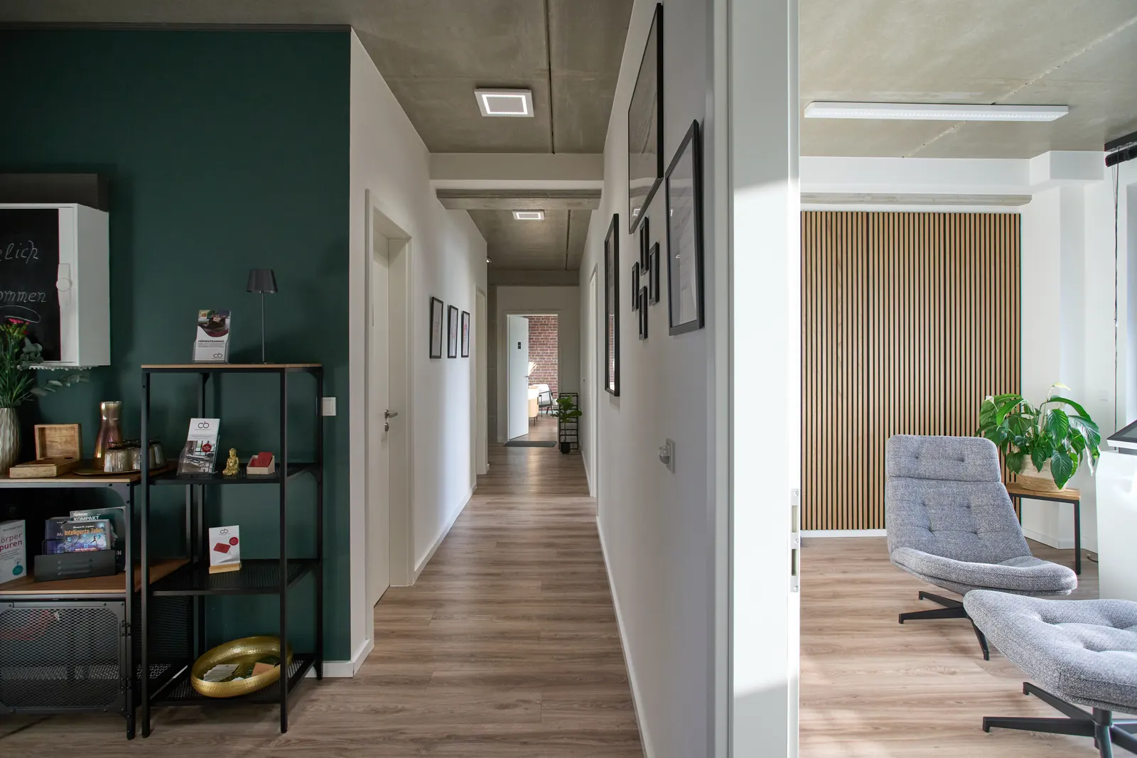 Blick durch den Praxisflur mit petrolfarbener Wand bis zum Sessel am Fenster