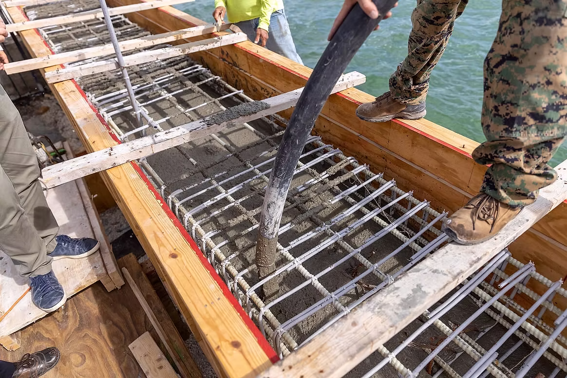 Concrete being placed by hose over a tied GFRP rebar mat in timber formwork on a waterside deck
