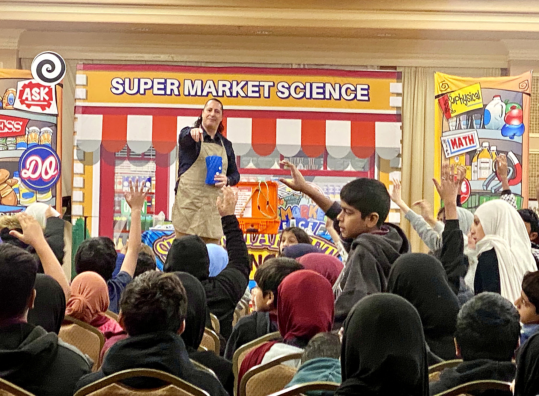 Children enthusiastically raising their hands during SuperMarket Science
