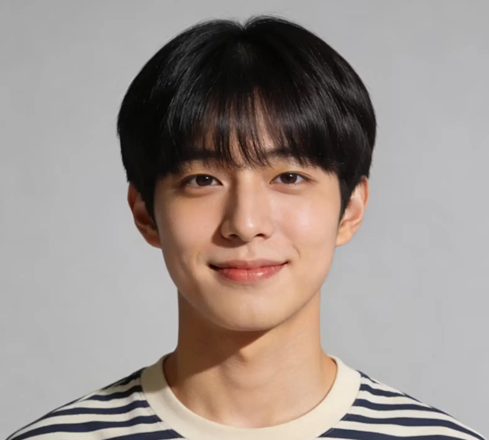 Young man with short black hair and bangs, wearing a white and black striped shirt, smiling softly against a plain gray background.