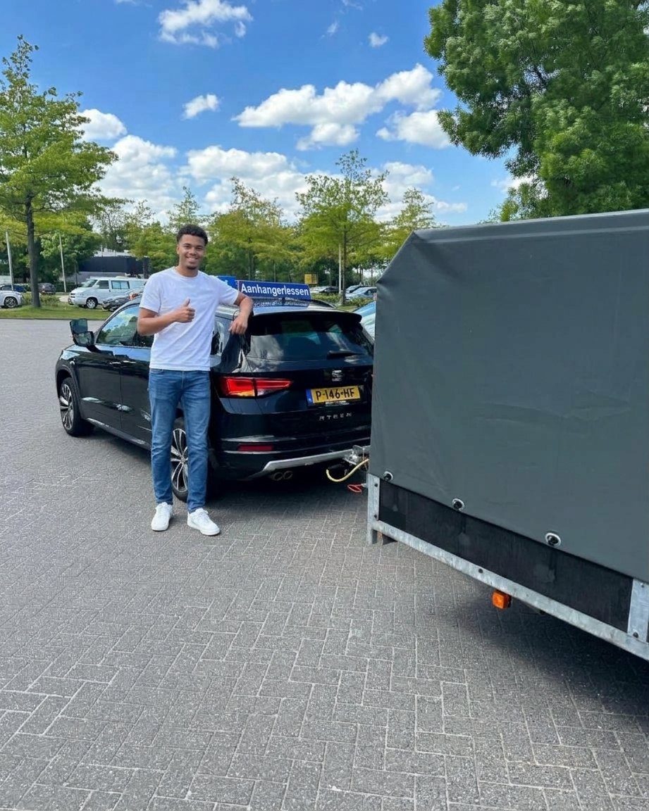 Leerling met duim omhoog naast de lesauto met aanhanger