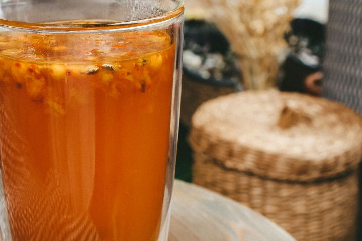 Pahar cu băutură portocalie de cătină, cu fructe plutind la suprafață