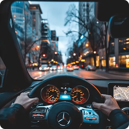 Person driving a Mercedes-Benz car in city traffic during dusk, dashboard and GPS screen visible.