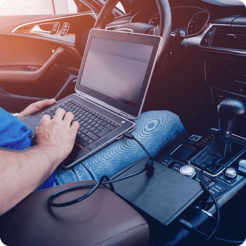 Person using a laptop connected to a diagnostic device inside a car with automatic transmission.