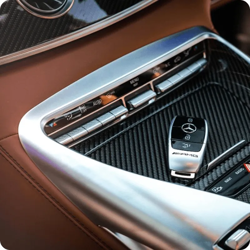 Car interior center console with carbon fiber trim, climate control buttons, and a Mercedes-Benz AMG key fob.