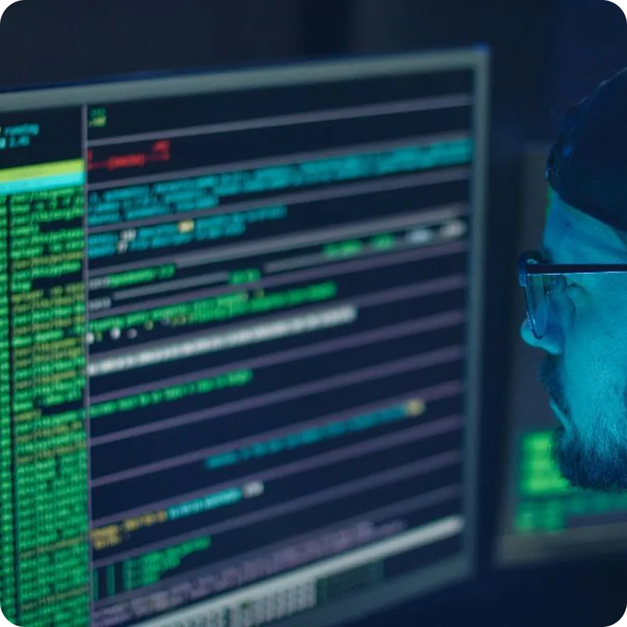 Person wearing glasses focused on a computer screen displaying blurred lines of code and data.