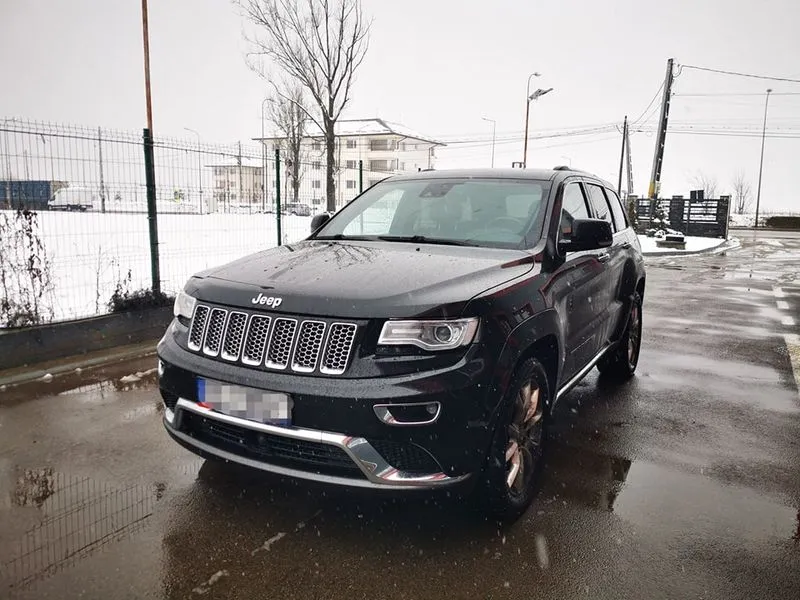 Black Jeep SUV parked on wet pavement with snow and bare trees in the background.