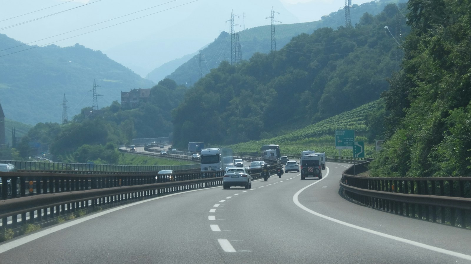 Camioane și autoturisme pe o autostradă printre dealuri cu vii
