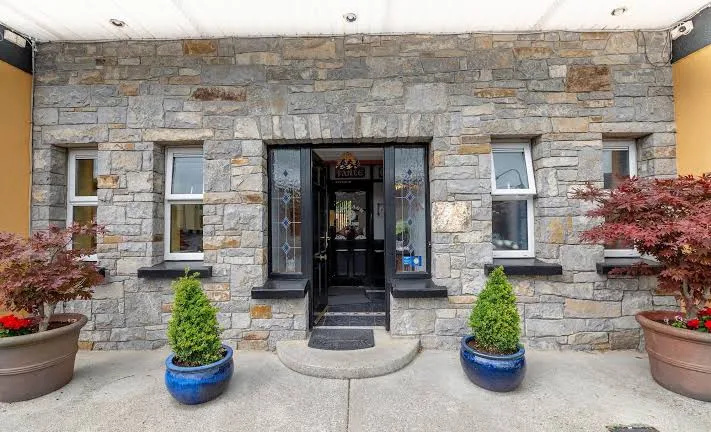 Stone facade of a building with a central glass door flanked by two windows, decorated with stained glass panels, and four large potted plants—two green shrubs in blue pots and two red-leafed plants in brown pots—symmetrically placed outside on a concrete surface.