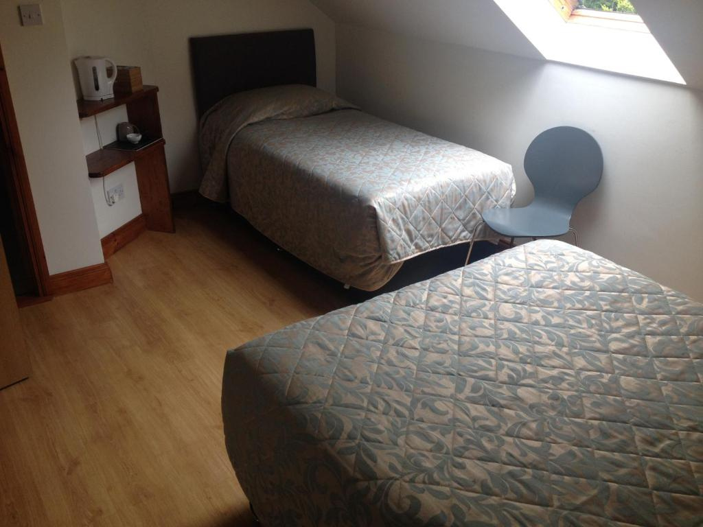 Simple bedroom with two single beds covered with patterned bedspreads, a blue modern chair near a slanted skylight window, and a small wooden shelf with a white kettle and cups.