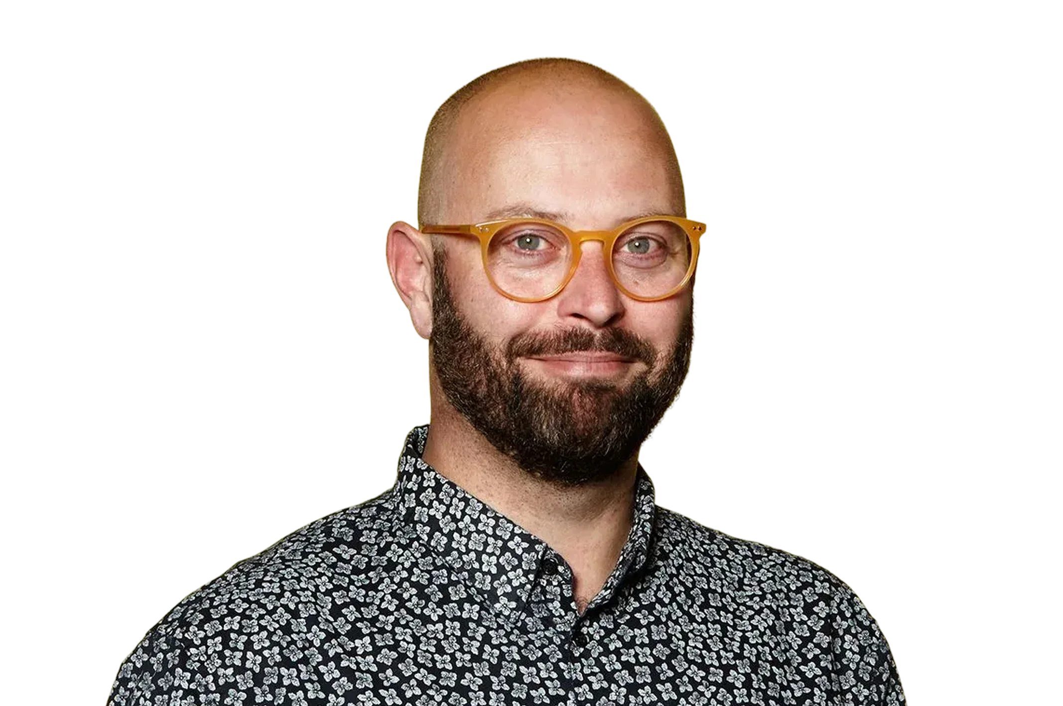 Smiling bald man with a beard wearing amber-colored round glasses and a black shirt with white floral patterns.