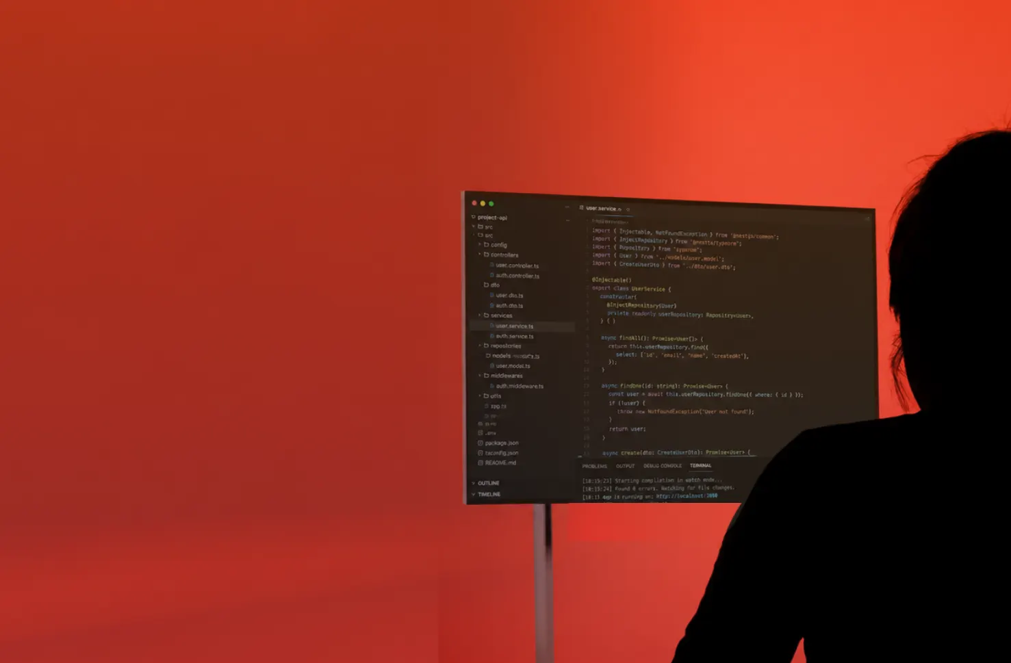 A person in silhouette facing a monitor of code against a red wall