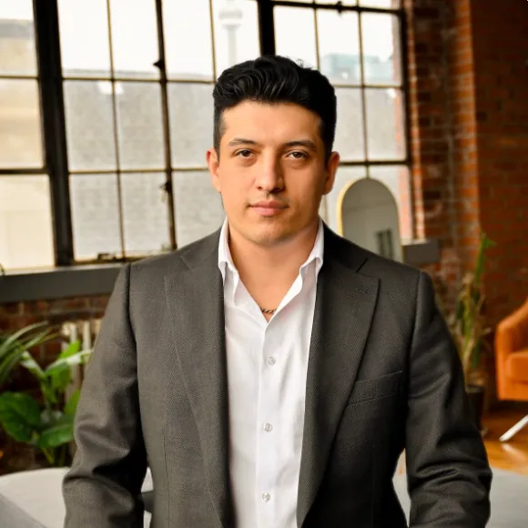 Portrait of Arman Tale in a dark blazer in a brick-walled office