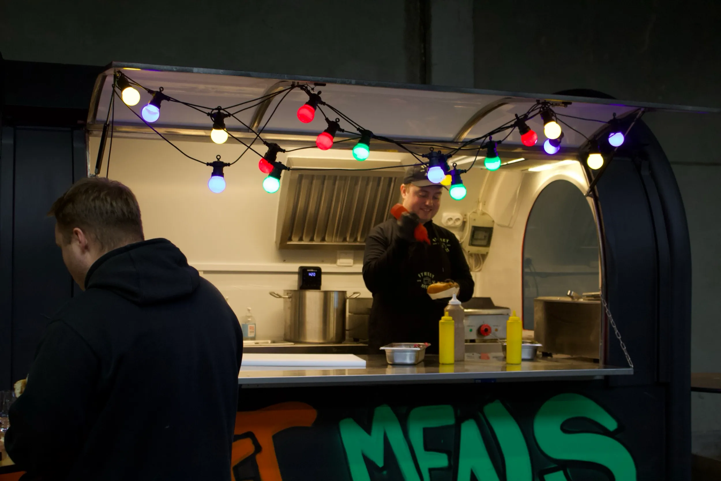 Kok serverer fra food trucken under kulørte lamper