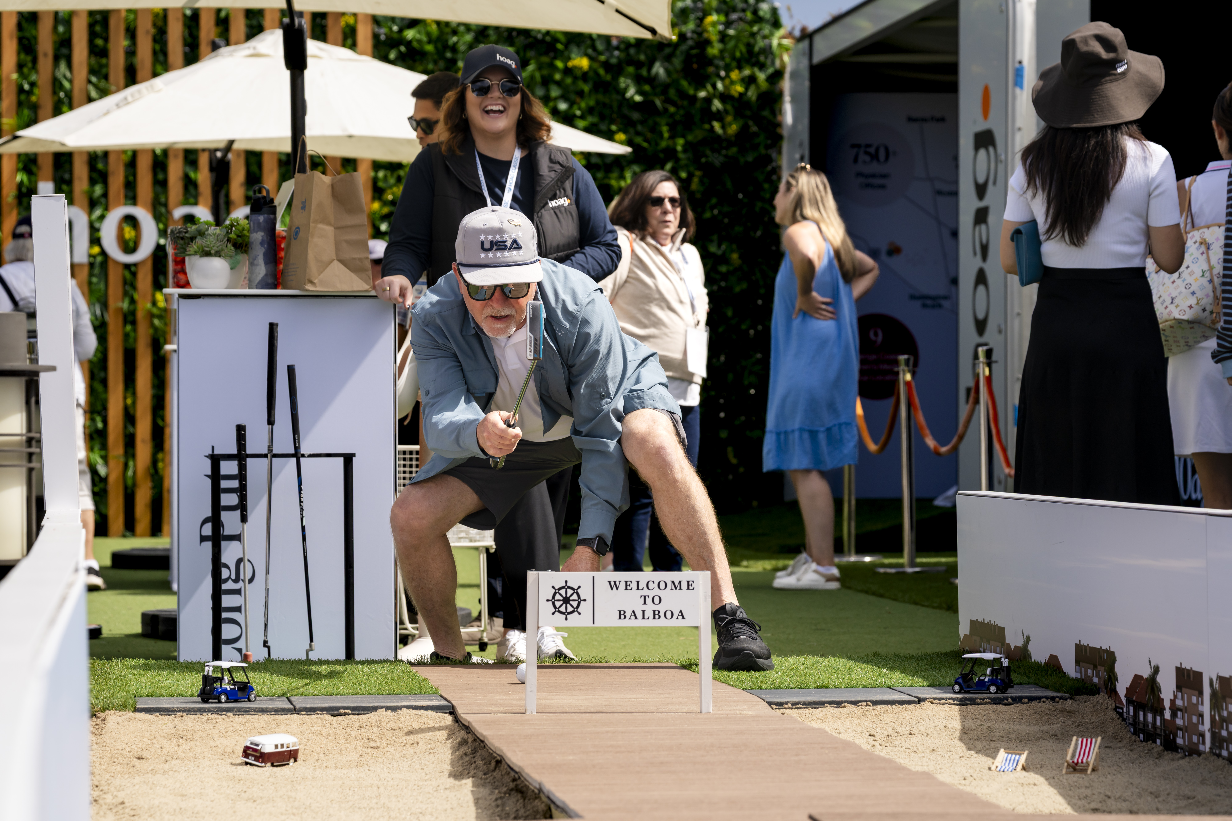 A guest lines up a putt at a hospitality putting game while a Hoag team member laughs behind him, Hoag Classic, Newport Beach