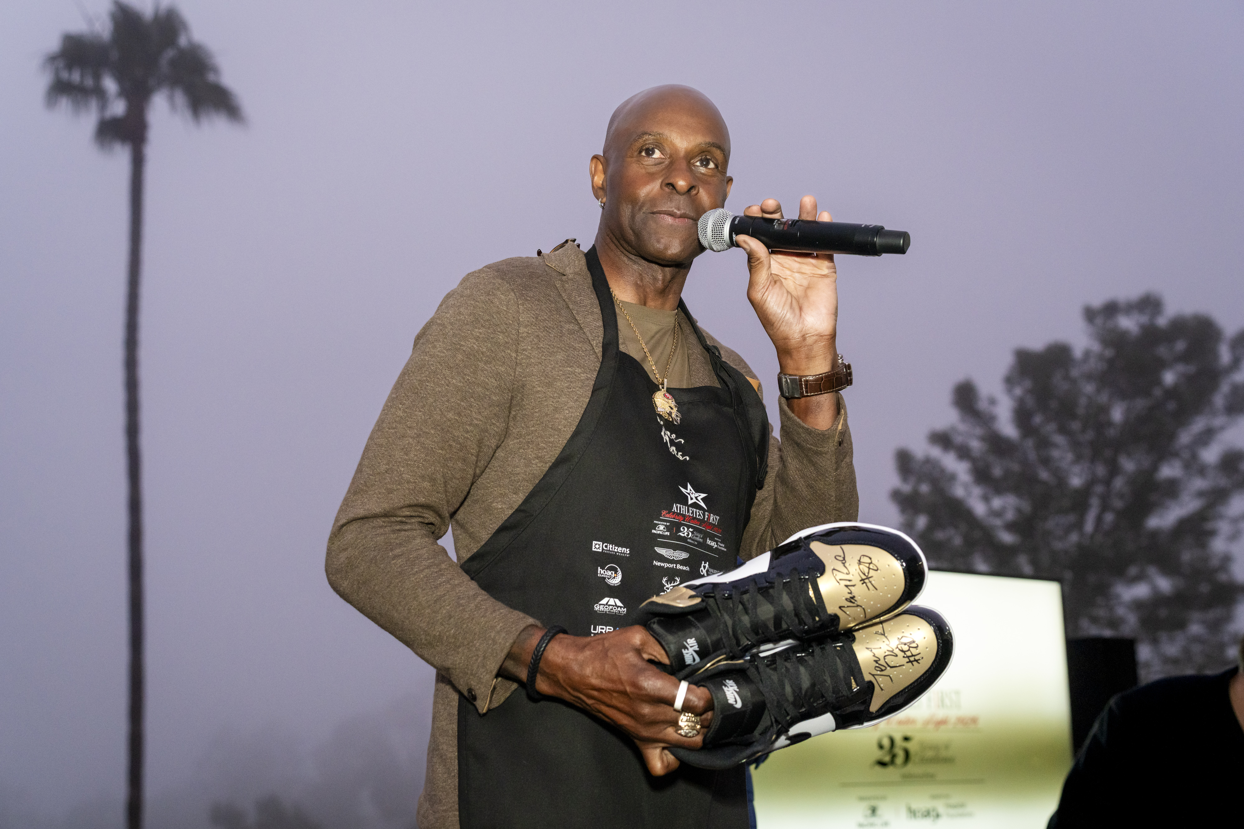 Jerry Rice on the microphone holding a pair of sneakers at a Hoag Classic 2026 evening event