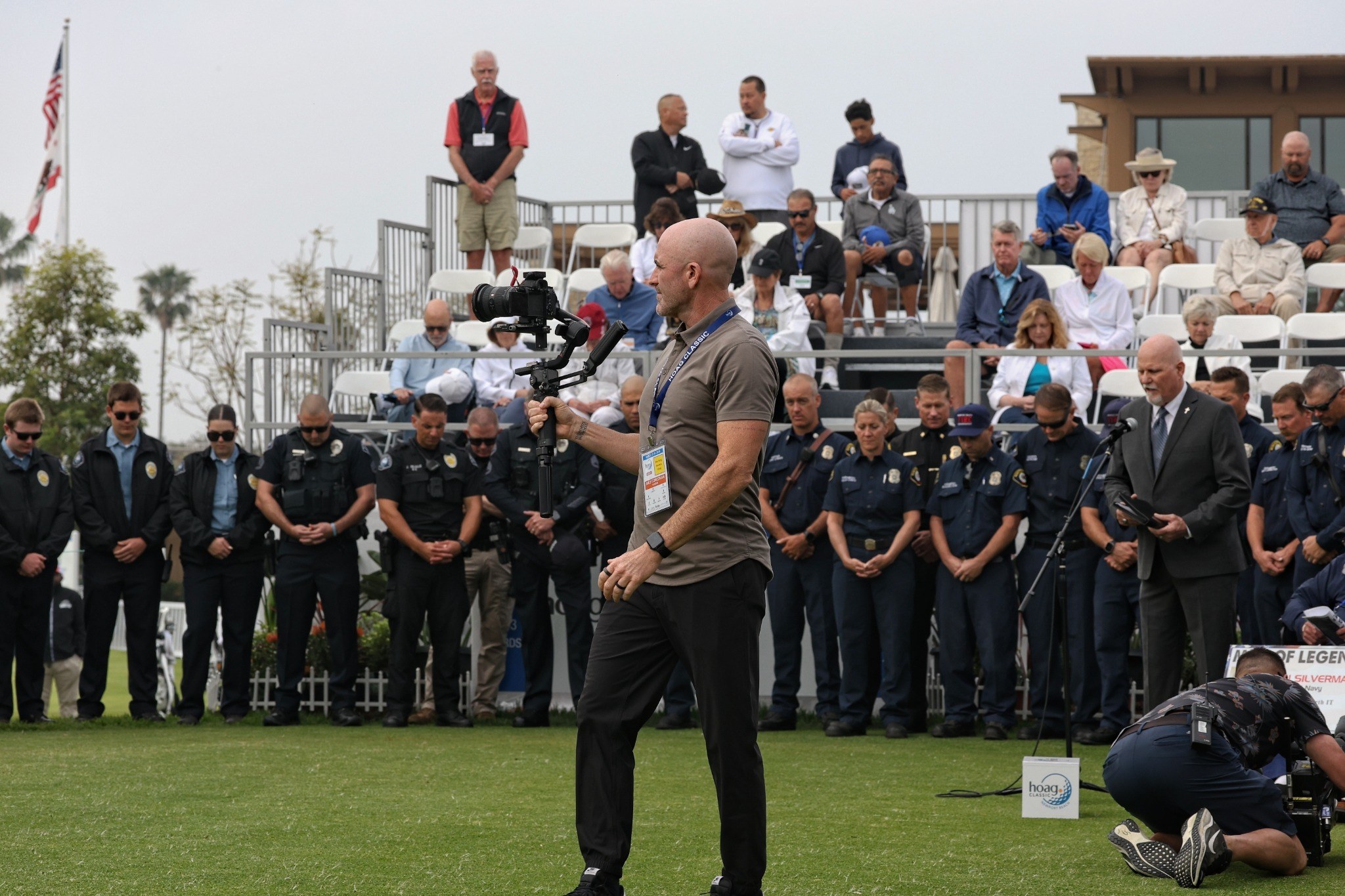 Billy Corcoran V filming on location at the Hoag Classic 2026, with police and fire personnel lined up behind him