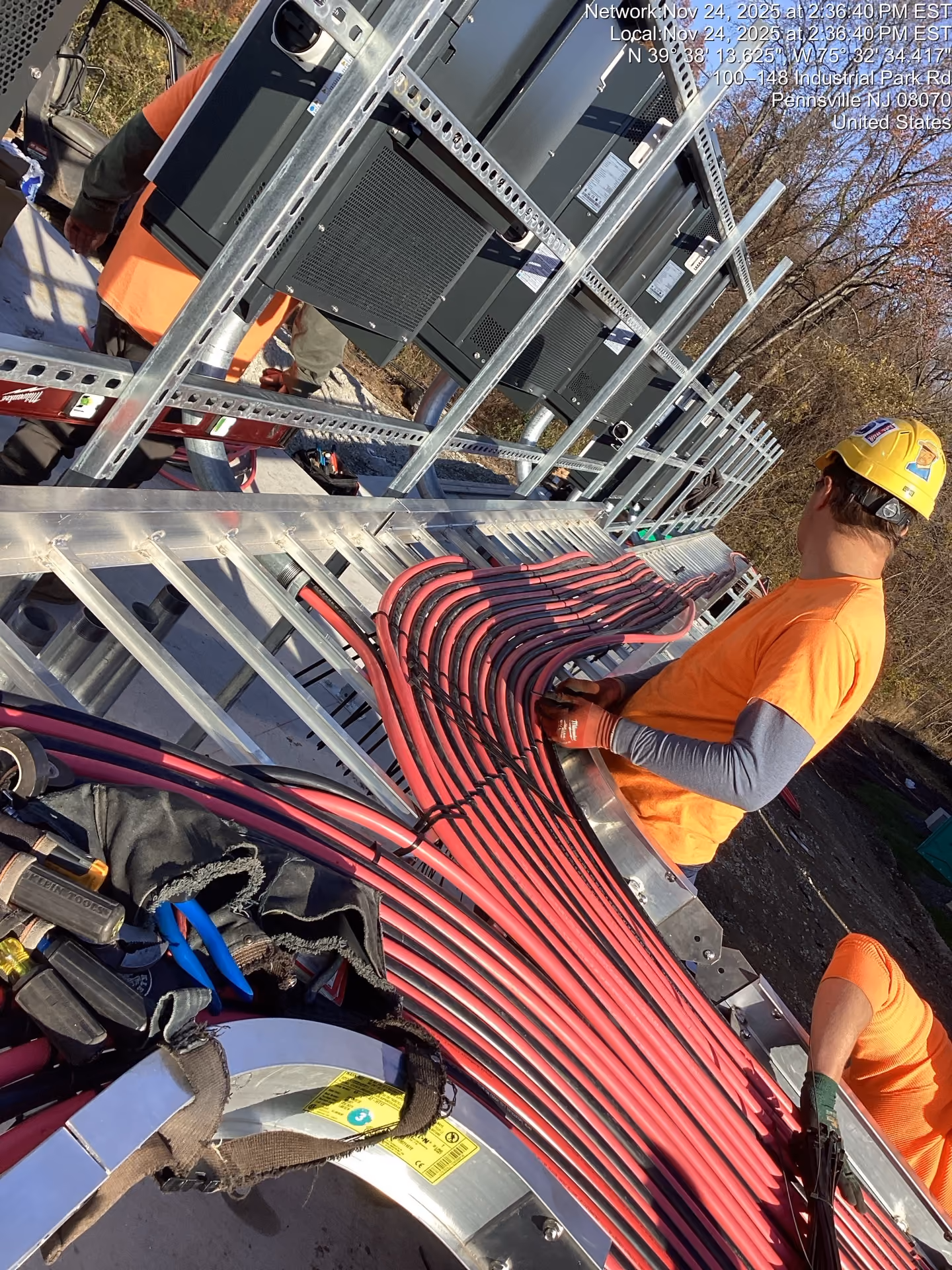 IBEW Local 351 electrician routing red feeder cables along a cable tray on a job site