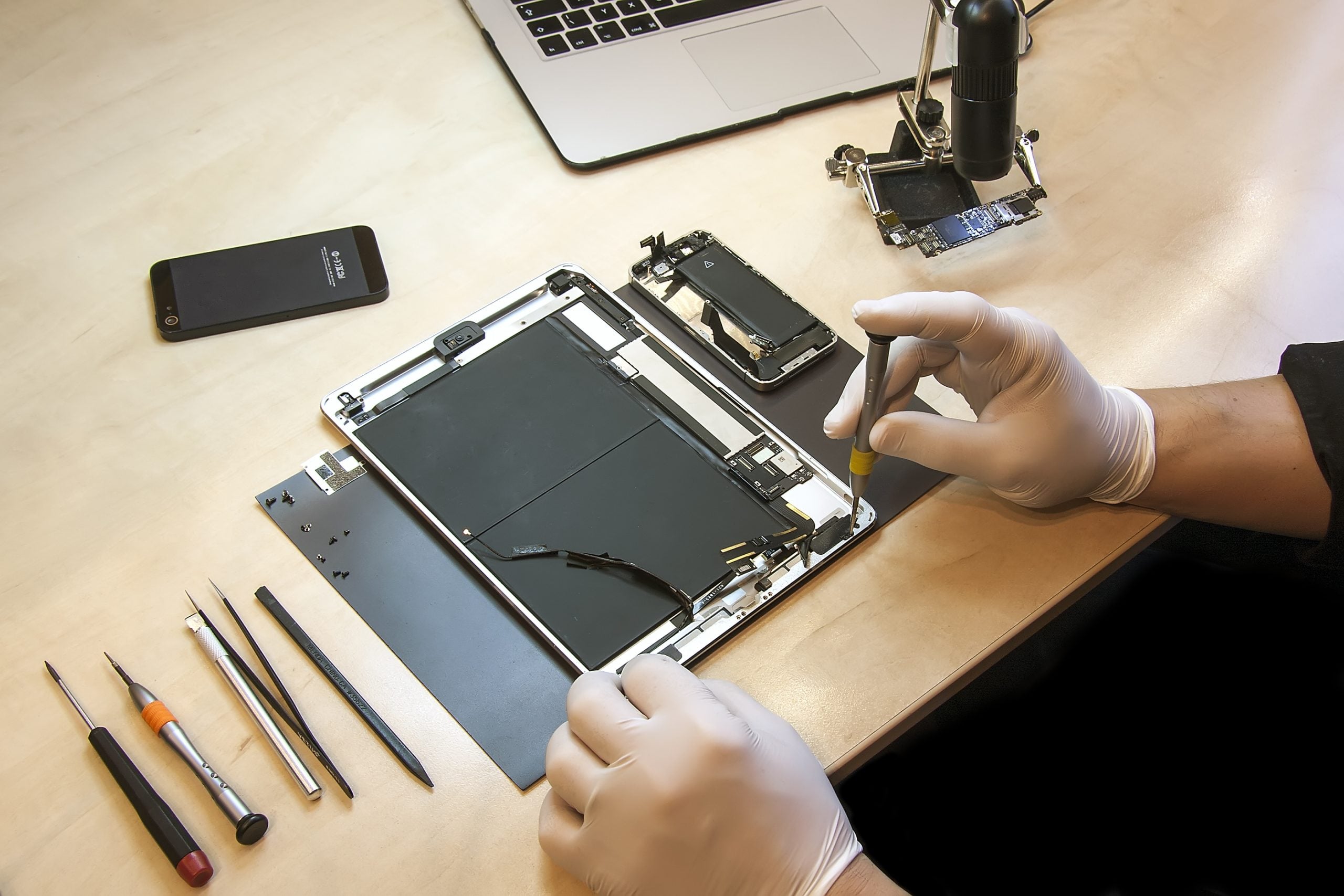 Technician in latex gloves disassembles tablet device with tools and components on wooden workstation