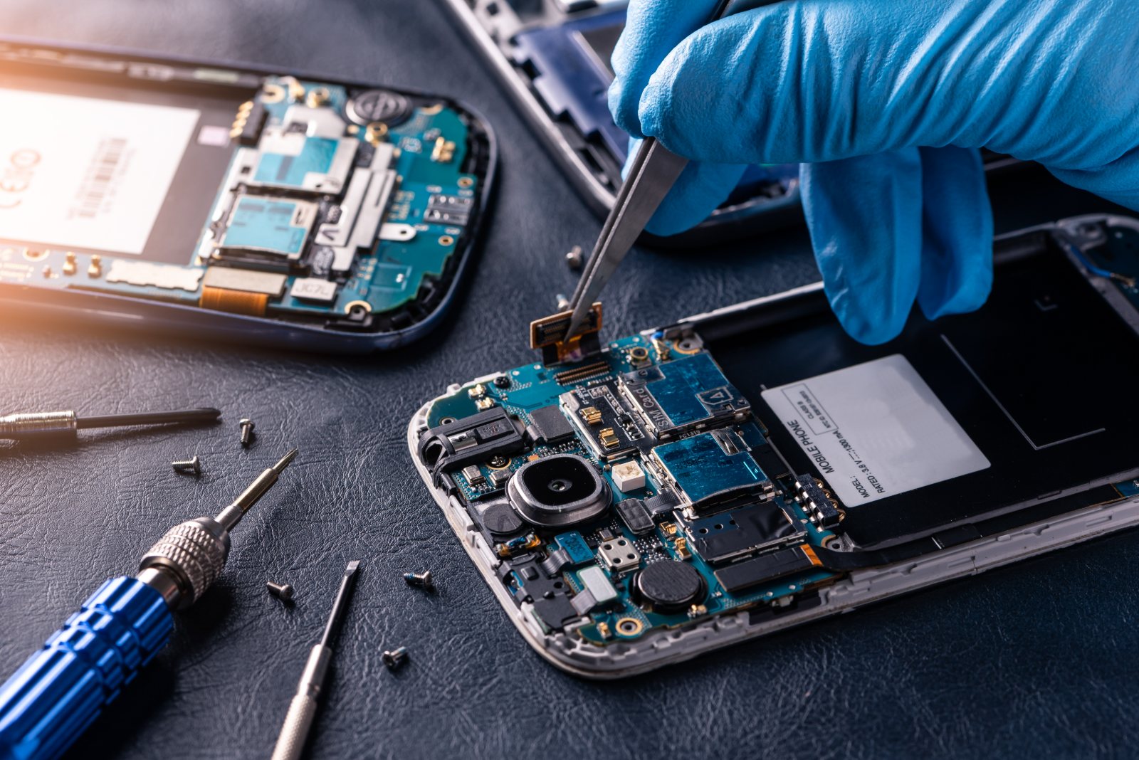 Technician in blue gloves repairing smartphone circuit board with screwdriver