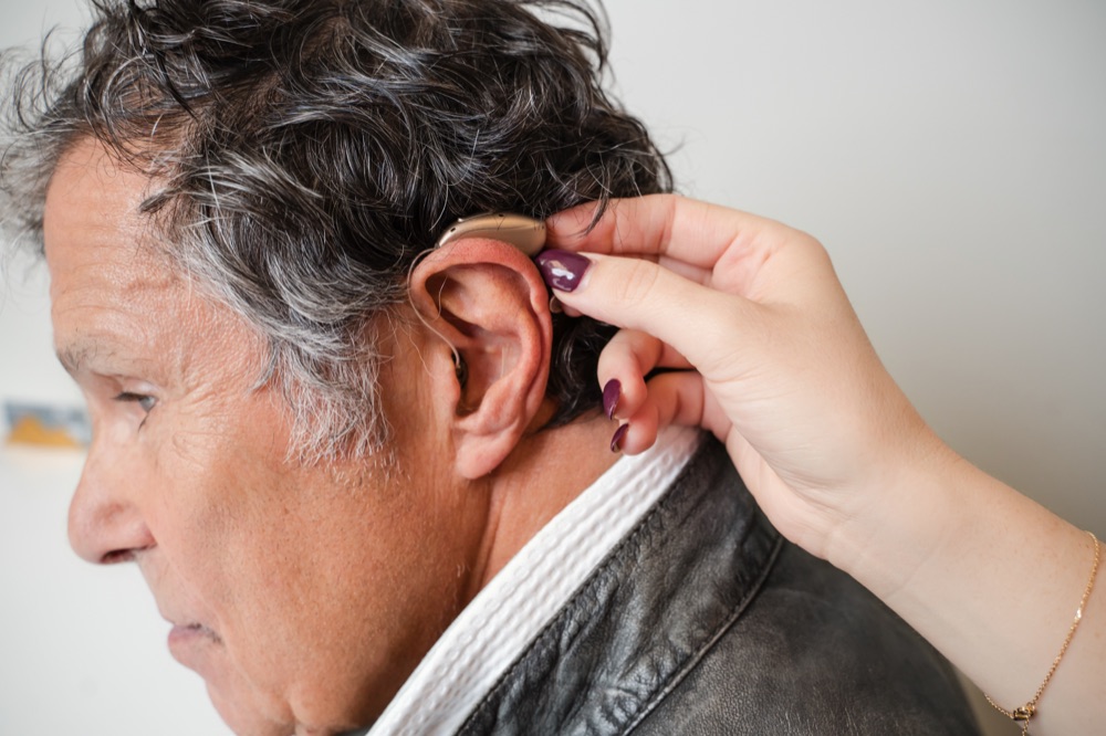 Close-up of a hand placing a hearing aid behind a patient's ear.