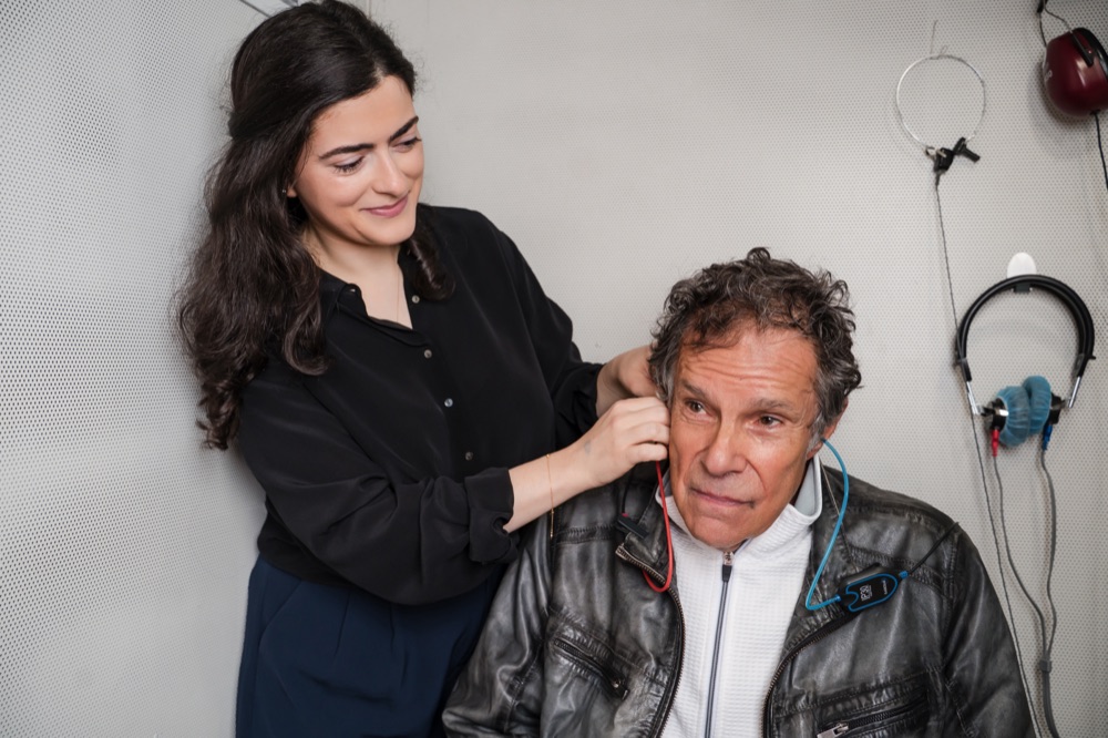 Dr. Melissa Patrich placing testing earphones on a patient inside a hearing test booth.