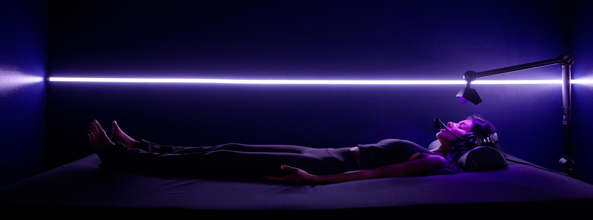 A guest lying on the WaveTable at Reality Center in Santa Monica, lit by a bar of violet light