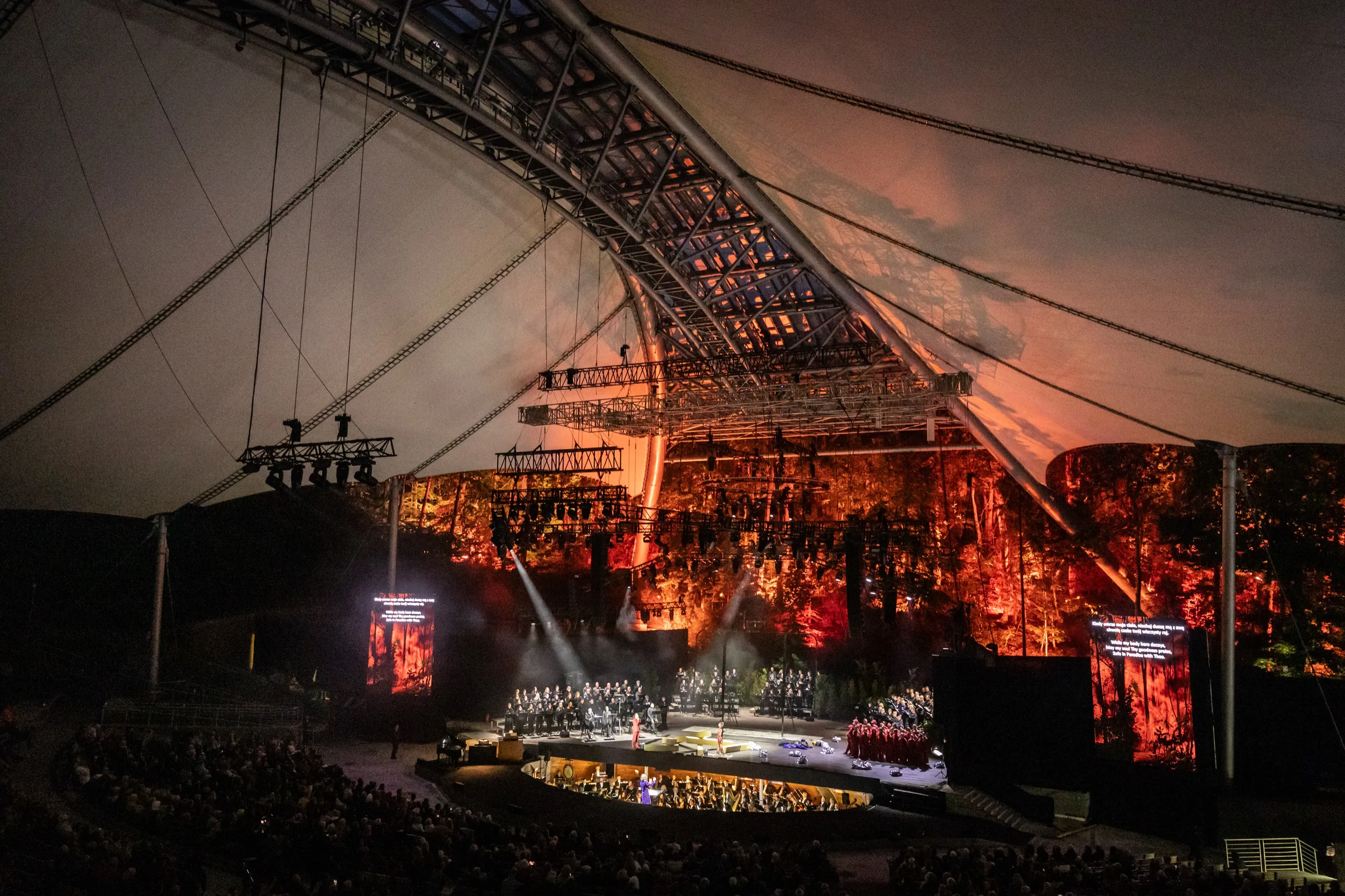 Orchestra and choir on the Forest Opera stage in Sopot, lit in orange, during the Baltic Opera Festival